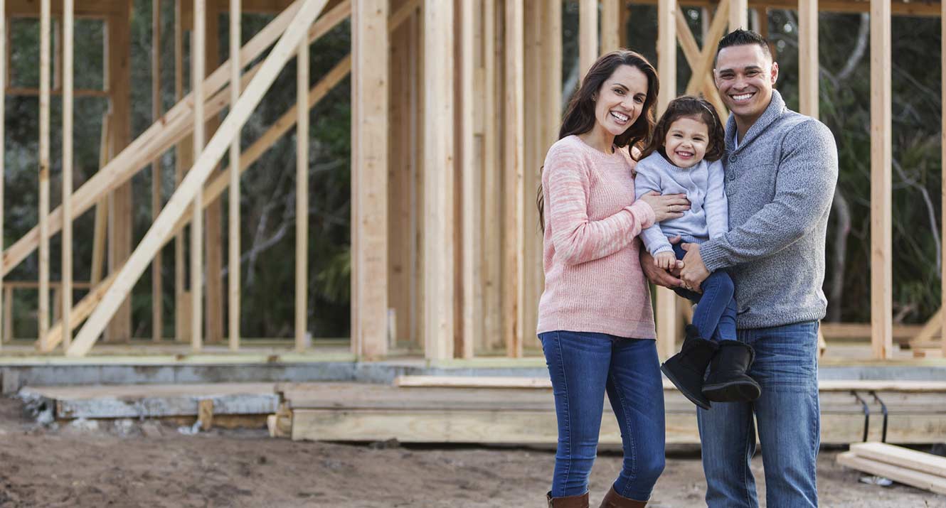 Young family standing in front of their new house being built.